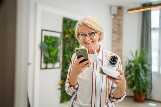 woman mature caucasian hold adjust home security camera and smartphone - Powered by Adobe