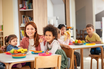 Happy preschool children of diverse backgrounds enjoying a healthy snack with their teacher in a bright and cheerful classroom setting.