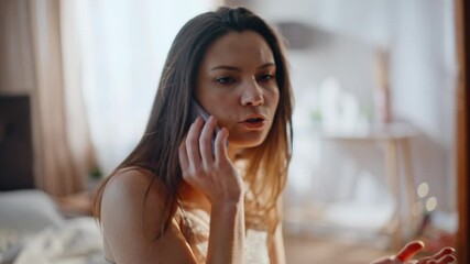 Concerned brunette talking mobile phone sitting home bed closeup. Woman calling
