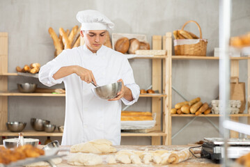 Young male bkery cook whisks chicken eggs to make dough in the bakery kitchen
