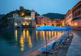 Obraz premium Peaceful evening view of a beach, blue umbrellas, and illuminated buildings reflecting in the waterfront.