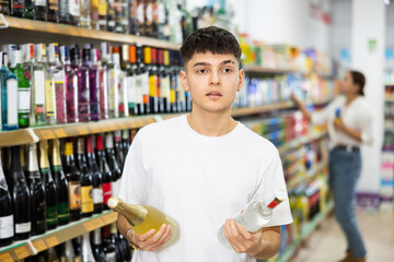 Young man looking to buy bottle of wine or vodka in supermarket
