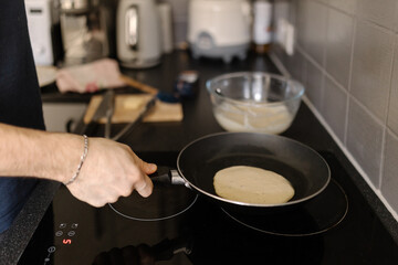 A close-up shot of a man preparing pancakes using a hot frying pan, soft focus.
