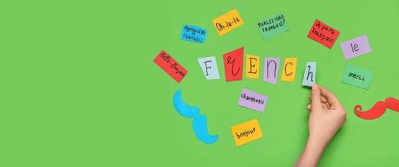 Hand and paper sheets with French words on green background with space for text