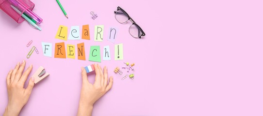 Hands with text LEARN FRENCH, glasses and different stationery on pink background with space for...