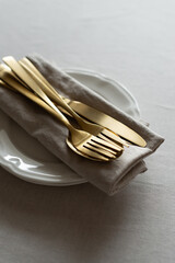 Golden cutlery with beige cotton napkins on the table. Knives, spoons and forks on a neutral cotton...