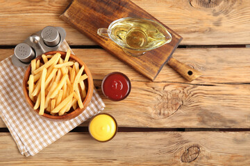 Bowl with tasty french fries, spices, sauces and oil on brown wooden background