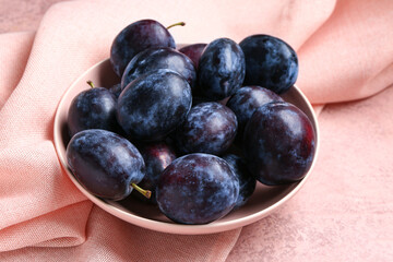 Bowl with fresh plums on pink background
