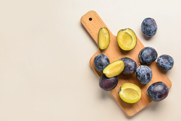 Wooden board with fresh plums on beige background