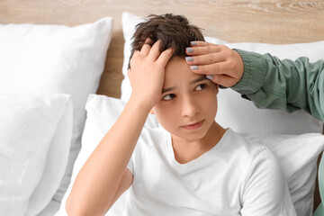 Mother touching forehead of her sick little son in bedroom, closeup