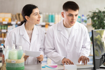 Two male and female pharmacists attentively stocktaking medicines with computer at small pharmacy shop