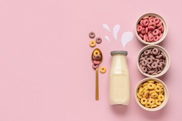 Bowls with colorful sweet cereal rings and bottle of milk on pink background