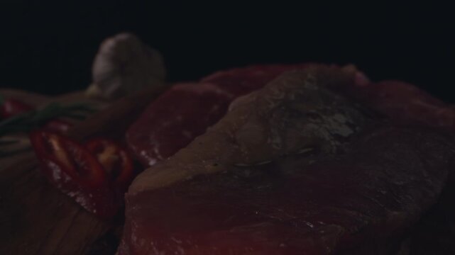 Chef preparing to cooking steak. Raw organic beef meat with rosemary, seasonings, salt and red pepper  on wooden cutting board, close-up. Slow motion