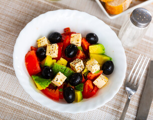 Just cooked avocado salad with chopped tomatoes, cheese feta served on plate with black olives.