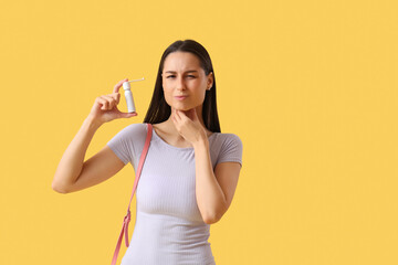 Young woman with spray for sore throat on yellow background