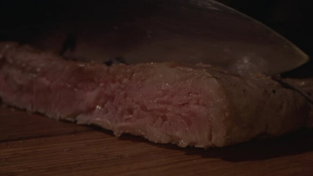 Male Chef hands cutting cooked beef steak with knife on wood cutting board, close up. Slow motion. Concepts food preparing process and restaurant service. 