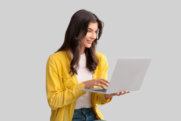 Fototapeta premium Beautiful young happy woman with laptop on grey background