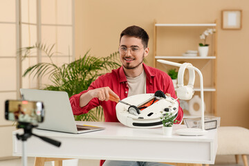 Young male blogger recording robot vacuum cleaner fixing tutorial at home