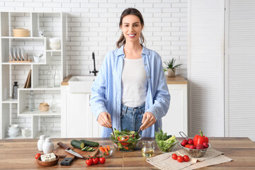 Beautiful young woman preparing fresh vegetable salad in kitchen