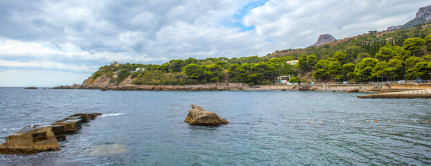 seascape of the coast of Foros in Crimea. In the center of the frame is a large stone foundation going into the water, and a separate rock on which a seagull sits. 