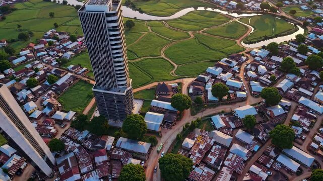 Aerial video capturing a vibrant cityscape with modern skyscrapers and lush green fields at sunset, showcasing urban and rural contrast.