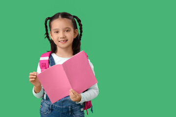 Cute little happy Asian girl with backpack and notebook on green background. End of school year