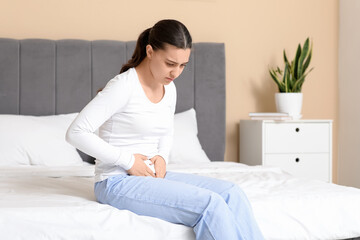 Young woman suffering from cystitis on bed at home