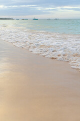 Waves gently lap against the serene sandy shore at sunset near the fishing boats in the distance