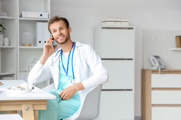 Male medical intern talking by mobile phone at table in clinic