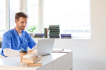 Male medical intern studying with laptop at table in library