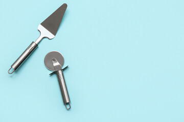 Stainless steel spatula and pizza cutter on color background