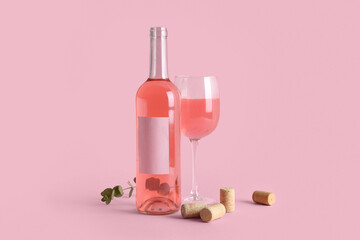 Glass and bottle of pink wine with eucalyptus twig and corks on pink background