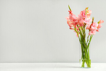 Glass vase with bouquet of beautiful gladiolus flowers on table against white background