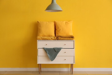 Pillows with folded blankets on commode near yellow wall in room