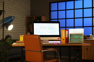 Computer monitor and laptop with codes on programmer's desk in dark office