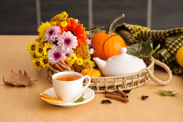 Wicker tray, tea pot, cup of hot green tea, flowers and autumn leaves on table in kitchen