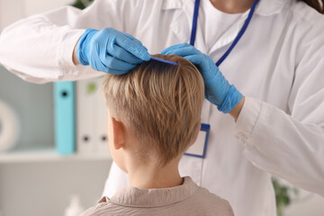 Female doctor brushing little boy's hair with pediculosis in clinic, closeup