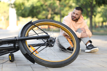 Young man with injured leg after falling off his bike in park