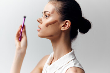 Profile of a young female model applying makeup with a brush, showcasing contour technique,...