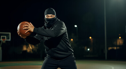 Young asian male basketball player in black outfit at night court with ball