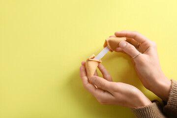 Female hands with broken fortune cookie on yellow background