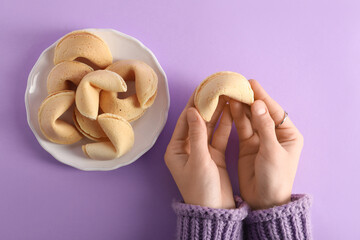Female hands with plate of fortune cookies on lilac background