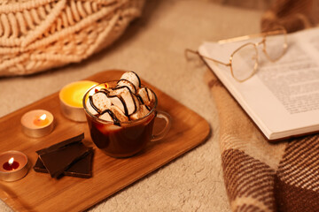 Cup of hot chocolate with marshmallows and book on wooden tray in room