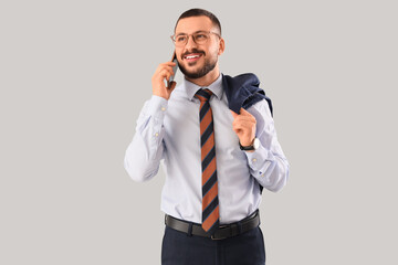 Young businessman with tie talking by mobile phone on light background