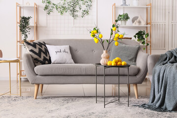 Lemon tree branches in vase on coffee table, sofa and armchair in interior of living room