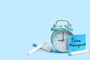 Sticky note with text TIME MANAGEMENT, alarm clock and markers on color background