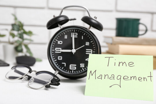 Paper sheet with text TIME MANAGEMENT, alarm clock and eyeglasses on light table