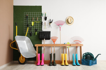 Gumboots and stand with gardening tools near colorful wall in barn