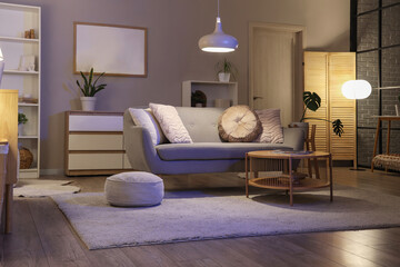 Interior of living room with grey sofa, table and glowing lamps in evening