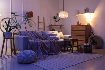 Interior of living room with sofa, bicycle and glowing lamps in evening